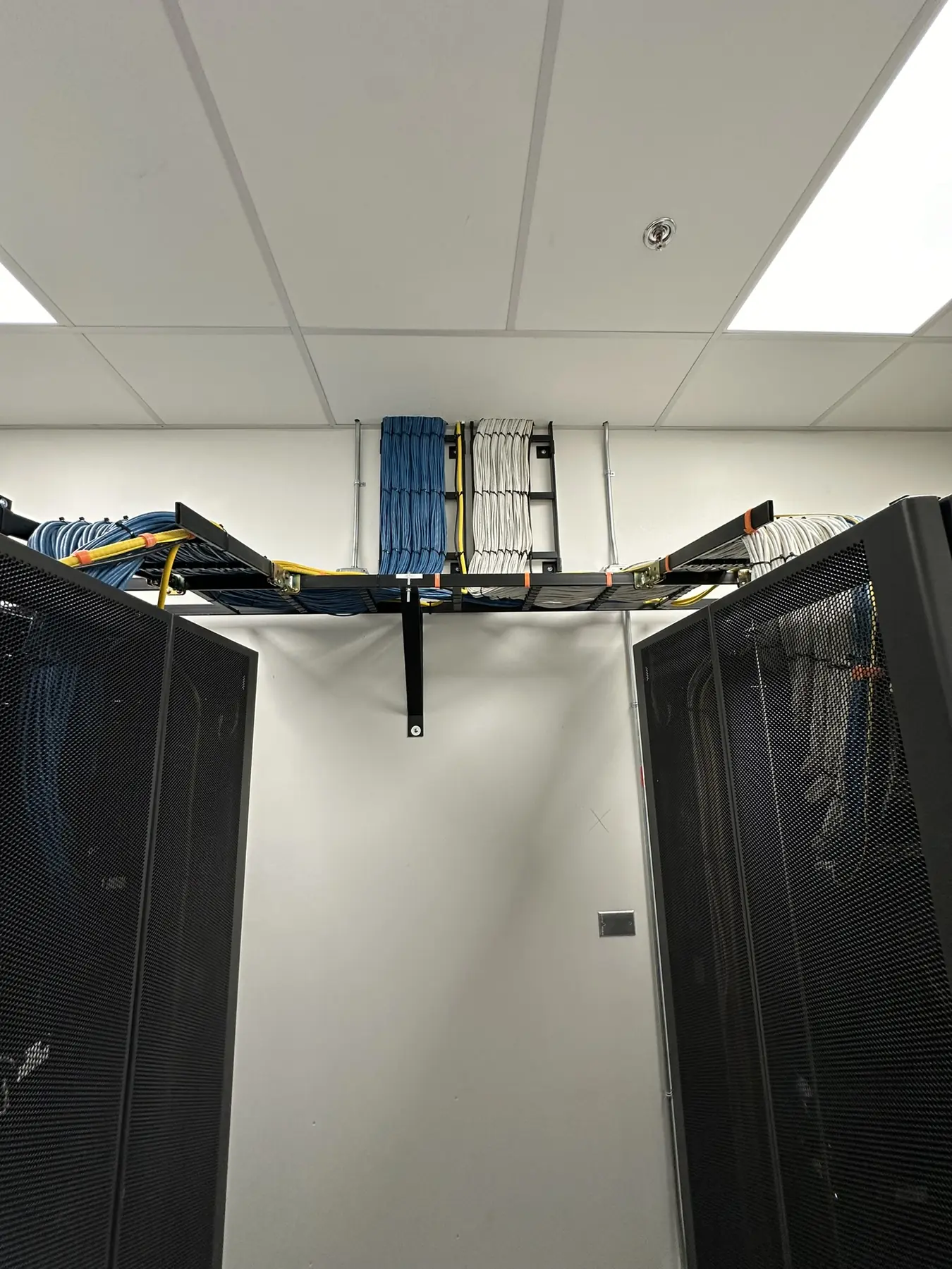 Blue and white structured cabling routed on overhead pathways between equipment cabinets